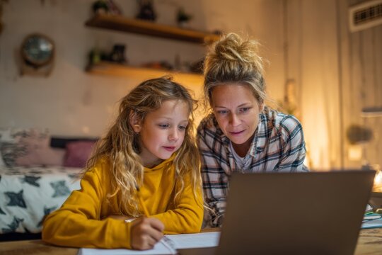 In a cozy study area filled with warm lighting, a parent assists a child with math problems during an online tutoring session