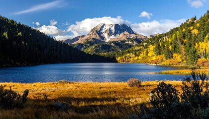 Naklejka premium A serene mountain lake reflecting a vibrant autumn landscape with golden grasses and colorful foliage framing a snow-capped peak.