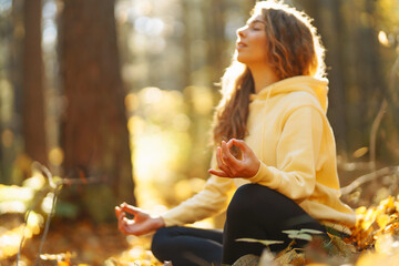 Relaxed woman practicing yoga poses, spreading arms in sunny autumn forest. Young woman enjoying...