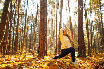 Relaxed woman practicing yoga poses, spreading arms in sunny autumn forest. Young woman enjoying...