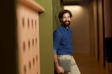 Smiling Professional Holding a Laptop in a Modern Business Environment