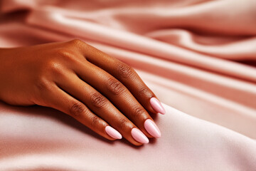 Hands with a classic French manicure are gently placed on luxurious, soft fabric. The delicate pink polish contrasts beautifully with the white tips, creating an elegant look