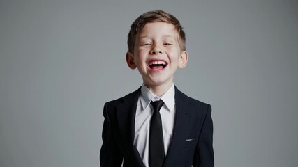 A young boy in a suit smiles confidently at the camera. The video captures a front-facing angle, emphasizing professionalism and charm.
