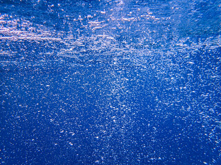 Underwater photography of the deep ocean with the ocean surface rippled with bokeh, bubbles, and...