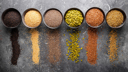 Pumpkin, sesame, flax, hemp, chia seeds in bowls, seeds for good health of mind and body, enriched with minerals and vitamins. Top view, grey background