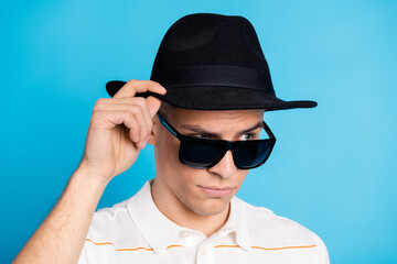 Portrait of a young man tipping his hat wearing sunglass, showcasing trendy and stylish flair against a bright blue background