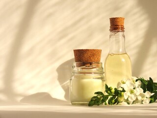 A small bottle of shower gel, a candle and a branch of white flowers and green leaves on a white background. A composition of self-care products for a moment of relaxation. Toiletries. Spa still life.