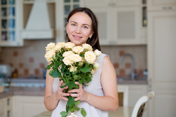 Young woman with long hair enjoying gifted yellow rose bouquet for Mother's Day in kitchen