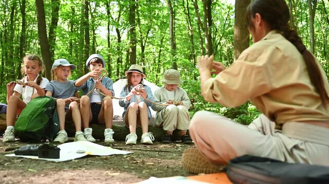 Teaching how to tie the knot. Woman is doing tour for group of kids in the forest.