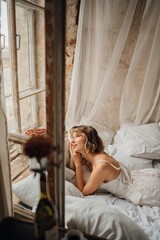 Obraz premium a young blonde woman in a white dress on white sheets by the window