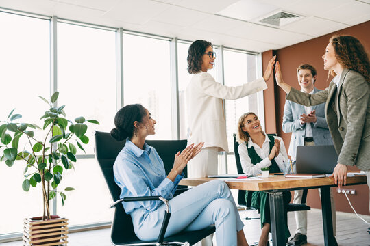 Diverse business team collaborating and celebrating with a high-five in a modern office space with positive energy - Powered by Adobe