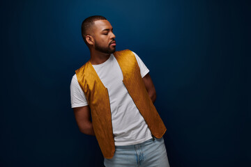 Confident young Black man in trendy outfit poses against a dark backdrop