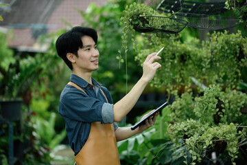 Portrait of an Asian man studying plants with technology in a vibrant outdoor nursery