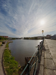 Mirandela, Portugal, viewed from the stone pedestrian bridge over the Tua River on a sunny August afternoon, 2025. Urban riverscape with distant water jet, tranquil setting.