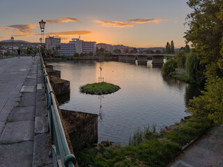 Pedestrian bridge over the Tua River in Mirandela, Portugal, leads to the city center at sunset. Evening light, calm water, and urban skyline create a tranquil and scenic connection.
