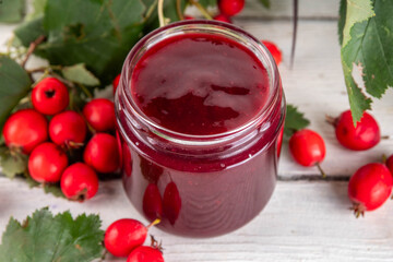 Wild forest hawthorn berry jam or marmalade in small jar with fresh berries on kitchen table, copy space