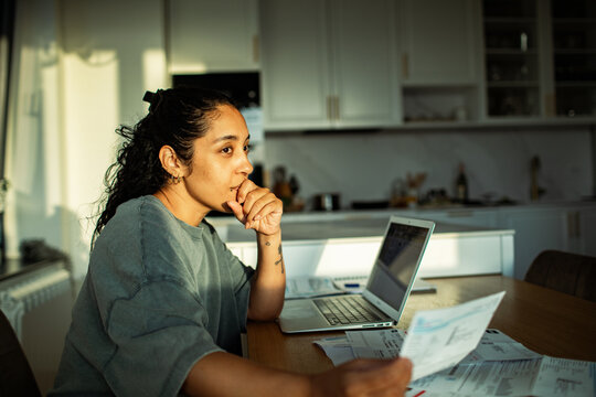 Young woman looking at bills with worried expression at home