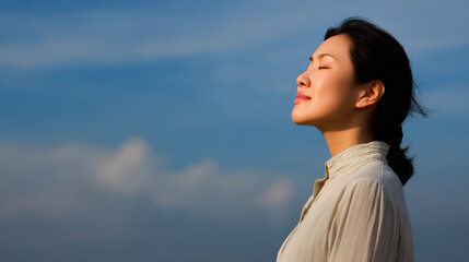woman peacefully closing her eyes in calm pose against clear blue sky with fluffy clouds