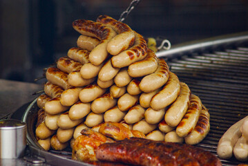 Delicious grilled sausages stacked in a pyramid shape on barbecue grill, traditional German bratwurst, tasty street food, Oktoberfest festival meal, assorted roasted meat, juicy hot pork sausages.