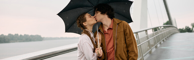 Young couple sharing a romantic kiss under an umbrella by the riverside