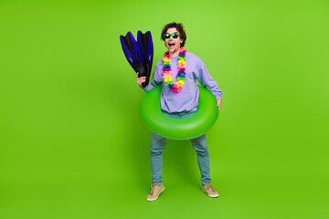 Young cheerful man with snorkeling gear and a green swim ring stands on a vibrant green background, ready for summer fun.