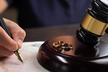 Close-up of a woman signing a divorce document next to a gavel and wedding ring in the background