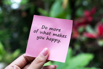 Hand holding a paper note with inspirational quotes do more of what makes you happy