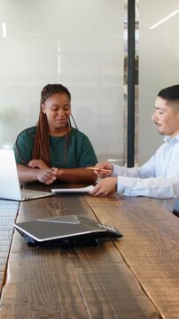 Vertical video: Diverse coworkers passing pen, signing documents at laptop, then shaking hands