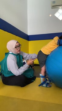 A compassionate physiotherapist assists a child with leg braces during physical therapy using an exercise ball, promoting mobility and development.