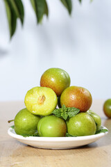 Fresh Green Plums with Red Flesh Cut Display on White Plate with Mint Garnish