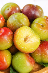 Fresh Red and Green Plums Cut Open Showing Golden Pulp with Water Drops on Wood