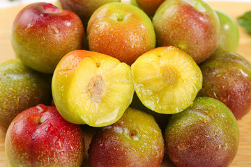 Fresh Red and Yellow Plums Cut in Half with Water Drops on Light Wood Background