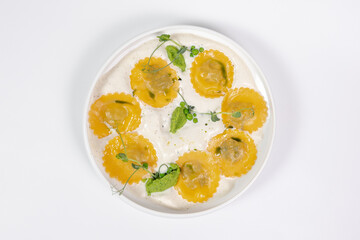 Top view of Ravioli in a creamy sauce with green puree and microgreens on a white background