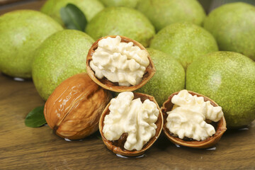 Fresh Green Walnuts with Cracked Shells Showing White Nutmeat on Wood Table Studio Photography