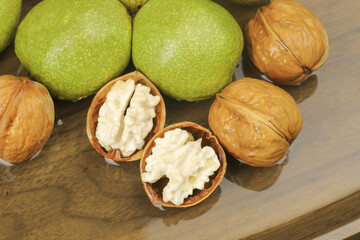 Fresh Walnuts with Green Husks and Cracked Shells on Wood Surface
