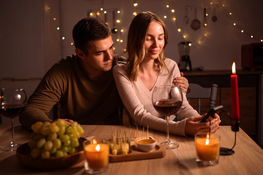 Happy young couple looking social media on smartphone during romantic dating in the kitchen at night. Valentine's Day
