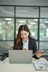  Asian businesswoman working at desk using laptop and notebook, talking with client or modern office building.