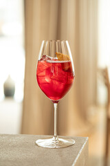 Red cocktail with orange slice and ice in elegant wine glass