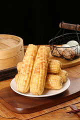 Fresh Sweet Corn Cobs on Plate with Traditional Bamboo Steamer and Wire Egg Basket on Wooden Table