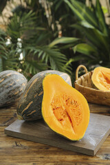 Fresh Orange Pumpkin Squash Cut in Half on Rustic Wooden Board with Wicker Basket and Tropical Garden Background