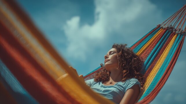 Young woman with curly hair relaxing with eyes closed in a colorful striped hammock on a sunny day under a clear blue sky