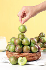 Fresh Green and Red Plums in Wicker Basket - Hand Picking Sweet Summer Stone Fruit on Yellow Background