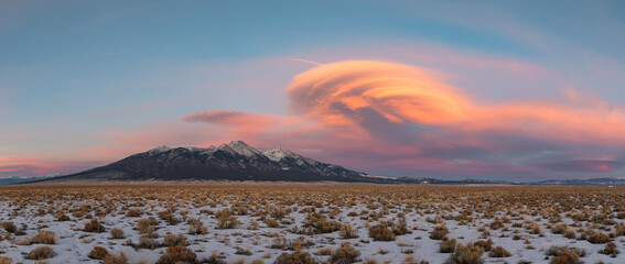 This winter mountain sunset panorama features a glowing colorful "spaceship" or lenticular cloud hovering over the snow covered Blanca Massif in Colorado's Sangre de Cristo mountains.