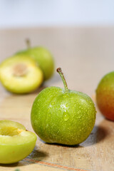 Fresh Green Plums with Water Droplets Cut and Whole on Wooden Surface