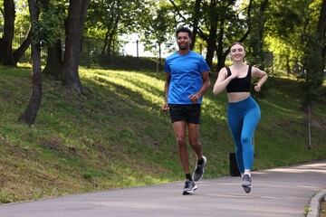 Obraz premium Smiling couple in sportswear running in park. Space for text