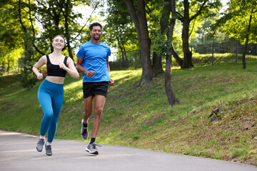 Obraz premium Smiling couple in sportswear running in park, low angle view. Space for text