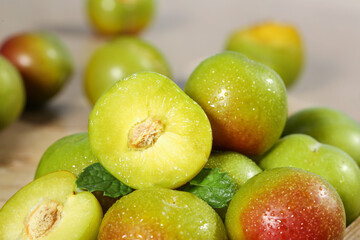 Fresh Cut Green Red Plums Halves Whole Fruit Mint Leaves Water Drops Light Wood Background