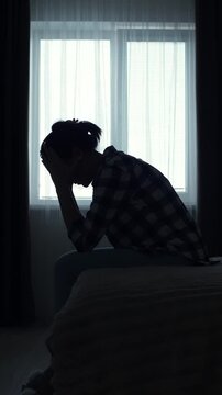 A woman&rsquo;s silhouette sits alone in a dark bedroom, deep in thought. She feels depressed, lost, and emotionally overwhelmed. A cinematic moment of inner struggle and mental health crisis.