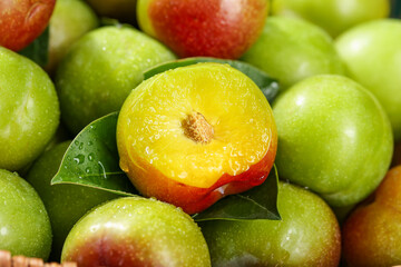 Cut Szechuan Plums Show Golden Pulp and Pit on Wood Surface with Fresh Green Leaves