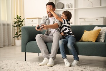 Father and son with controllers having fun while playing videogame on sofa at home